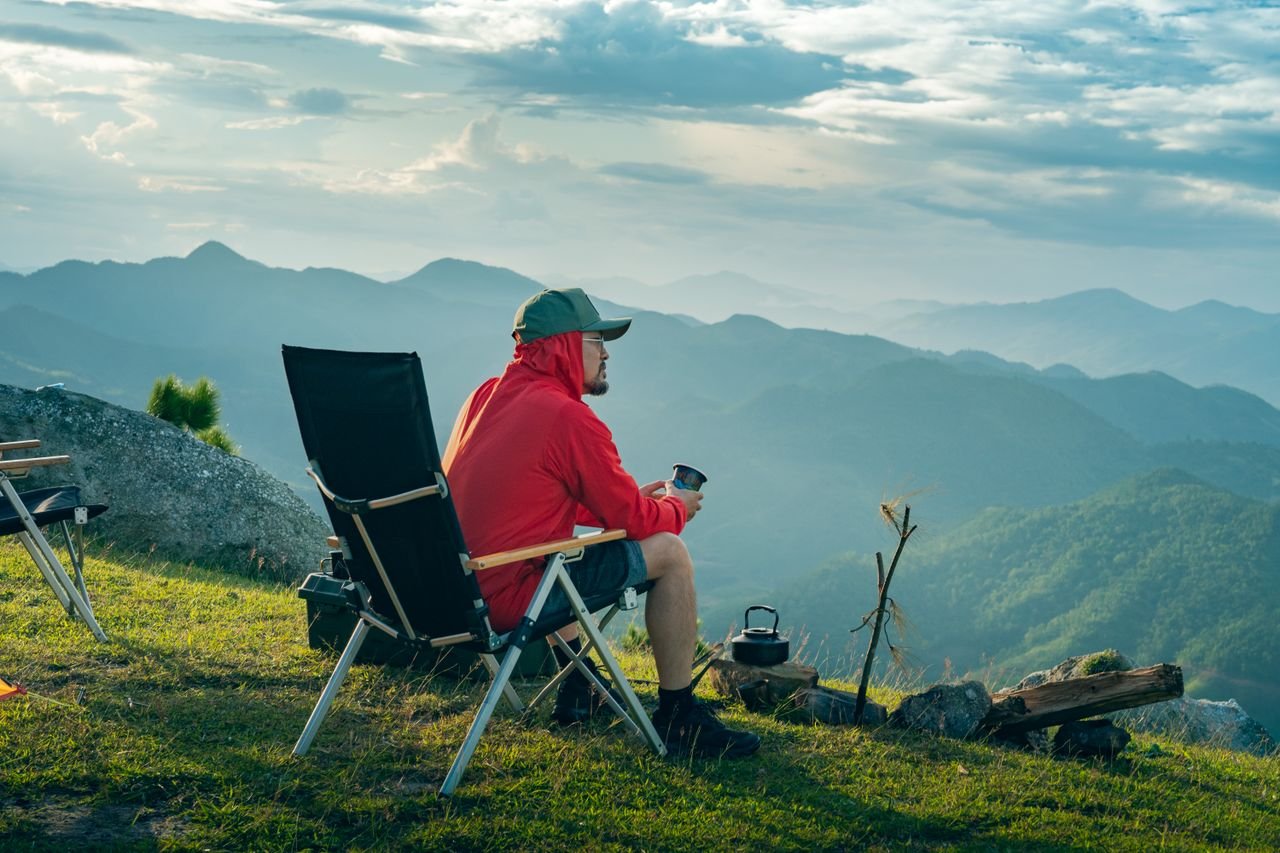 Man enjoys quiet mountain sunrise with campfire. Perfect nature escape.